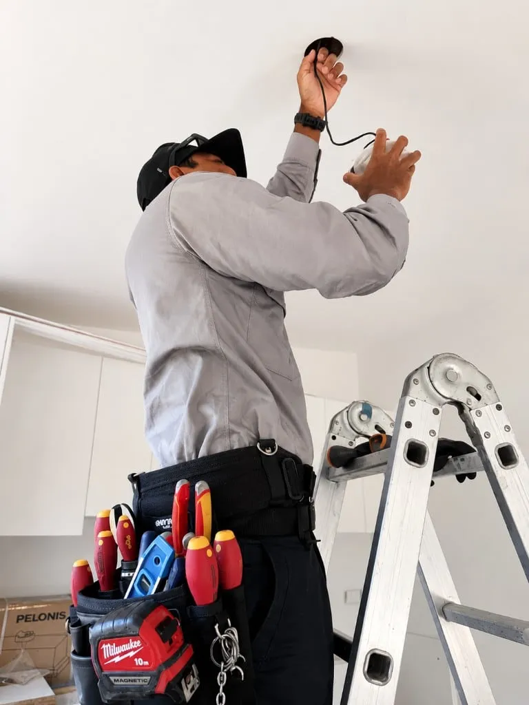 PQ electrician on a ladder wiring a downlight into a Brisbane ceiling